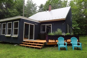 A dark blue house with a metal roof, a deck, and two Adirondack chairs.