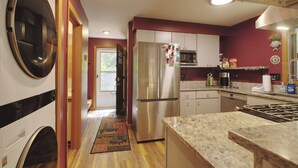 A kitchen with a stainless steel refrigerator, microwave, and stove, wooden flooring, and a view into the adjacent living area. - Cozy Private Single Family Home, Campton NH-MV118C (Campton)