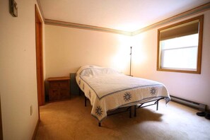 Une chambre à coucher comprenant un lit, une table de chevet, une commode, une fenêtre et un radiateur.