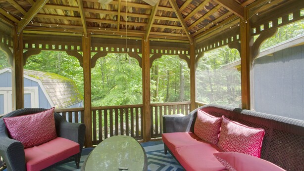 A covered outdoor seating area with wooden beams, a ceiling fan, and a view of a forested area. - Cozy Private Single Family Home, Campton NH-MV118C (Campton)