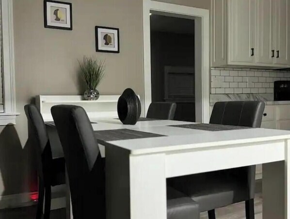 A modern kitchen with white cabinets, a dining table with black chairs, and framed artwork on the wall.