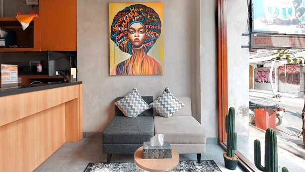 A modern living room with a sofa, two patterned cushions, a coffee table with a tissue box, a painting on the wall, and a cactus on the windowsill. - dBeds Kuta Beach (Kuta)