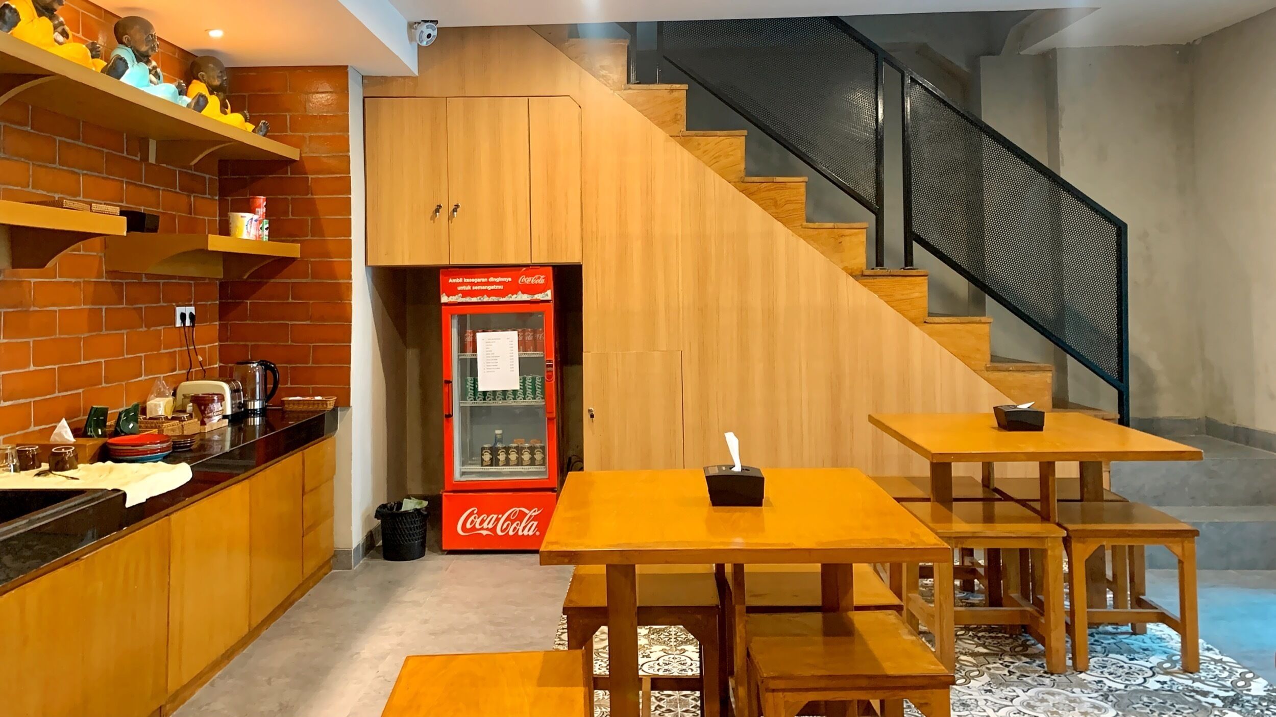 A kitchen with wooden cabinets, a brick wall, a Coca-Cola refrigerator, and a staircase with a metal railing.