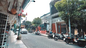 A street with parked motorcycles and a white car. There are buildings with signs, including one that says "RENTAL." - dBeds Kuta Beach (Kuta)