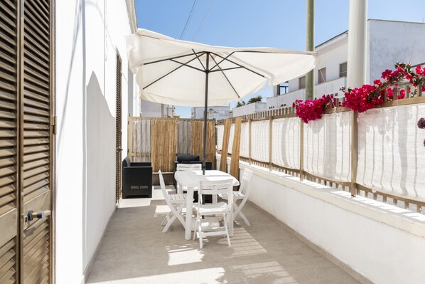 Une terrasse avec une table et des chaises, un parasol blanc et une clôture en bambou ornée de fleurs.
