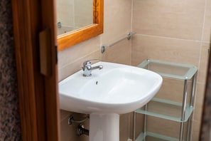 A bathroom with a white sink, a wooden-framed mirror, and a glass shelf unit.