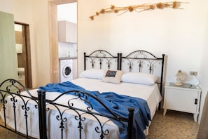 A bedroom with a metal bed frame, a washing machine, a bedside table with a lamp, and a wall-mounted decoration.