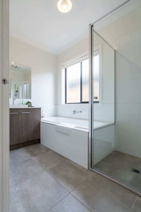 A bathroom with a glass shower enclosure, a white bathtub, and a vanity with a mirror.