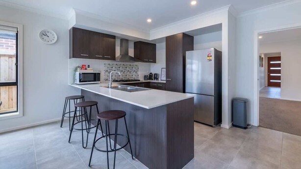 Una cocina moderna con una isla central, armarios oscuros, un refrigerador de acero inoxidable y un microondas.
