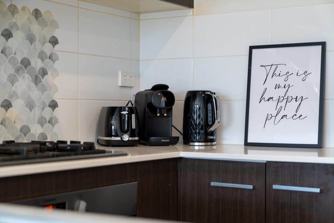 Eine Küche mit Kaffeemaschine, Wasserkocher und einem gerahmten Schild an der Wand.