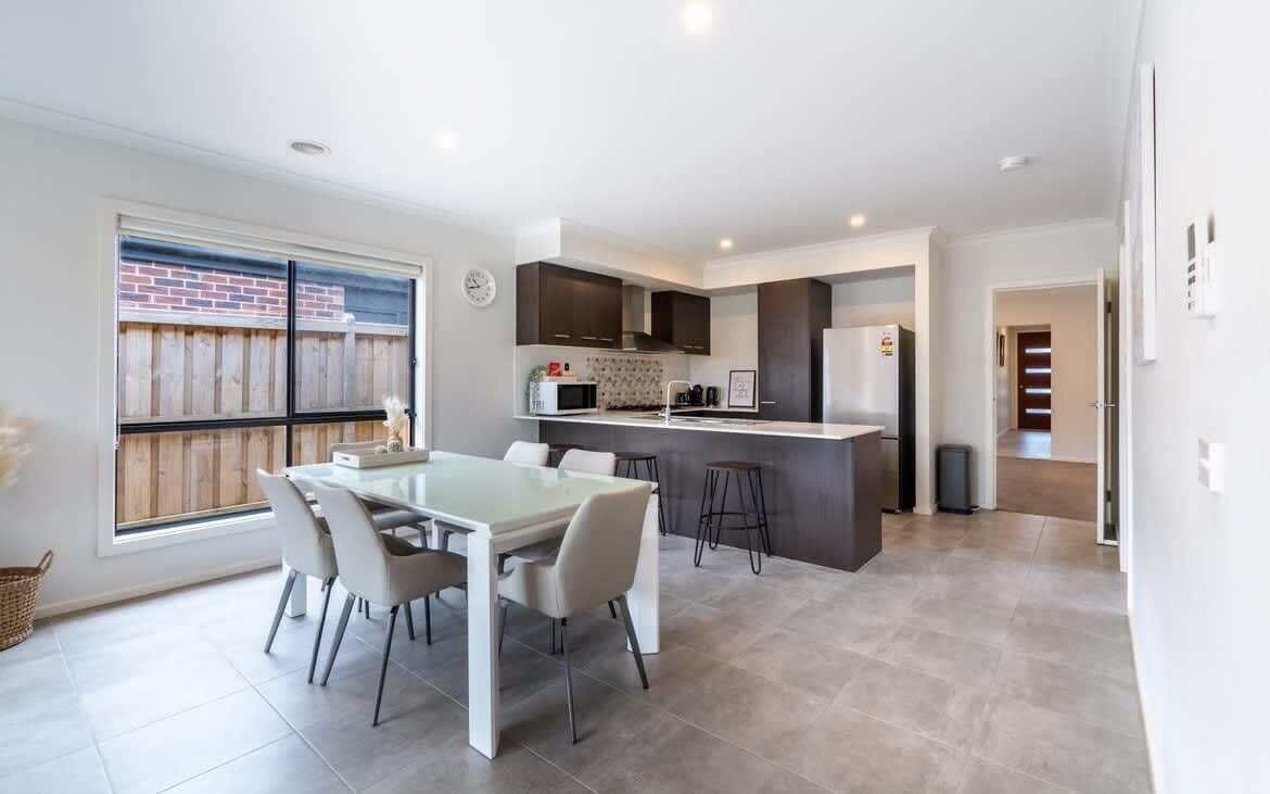 A modern kitchen with a dining area, a large window, and a view of the backyard.