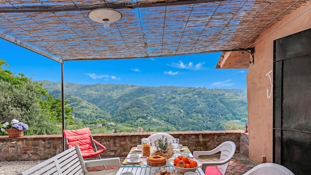 A table set outdoors with a scenic mountain view, white chairs, and a variety of food items. - Villa Ortensie Garden with Amazing View (Marliana)