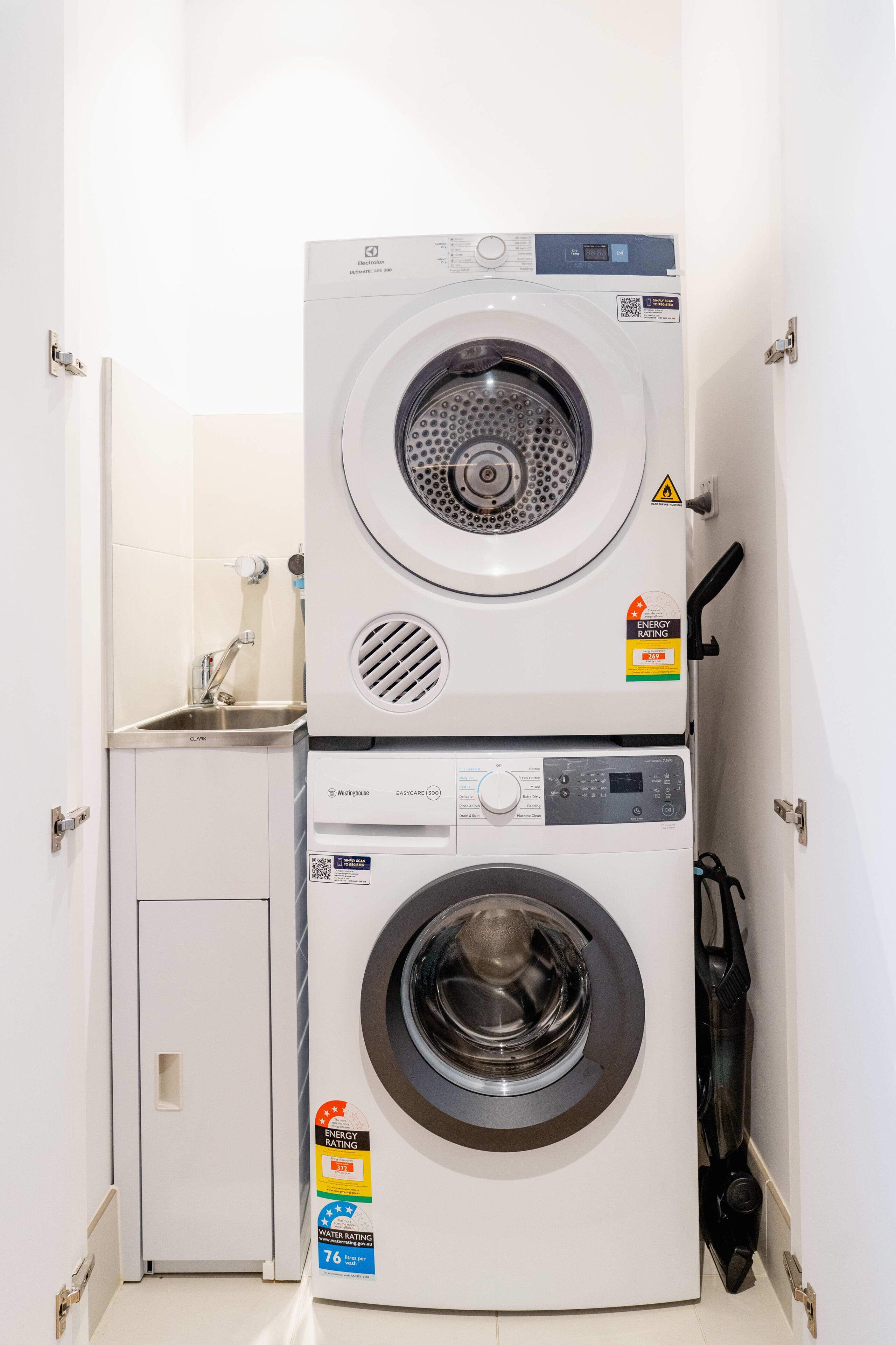 Une petite buanderie équipée d’un lave-linge et d’un sèche-linge à chargement frontal, d’un petit évier et d’une porte.