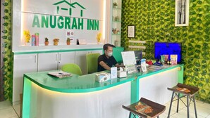 A reception desk at Anugrah Inn with a green leafy wall design, a clock, and a computer monitor. - ANUGRAH INN HOTEL (Ciakar)