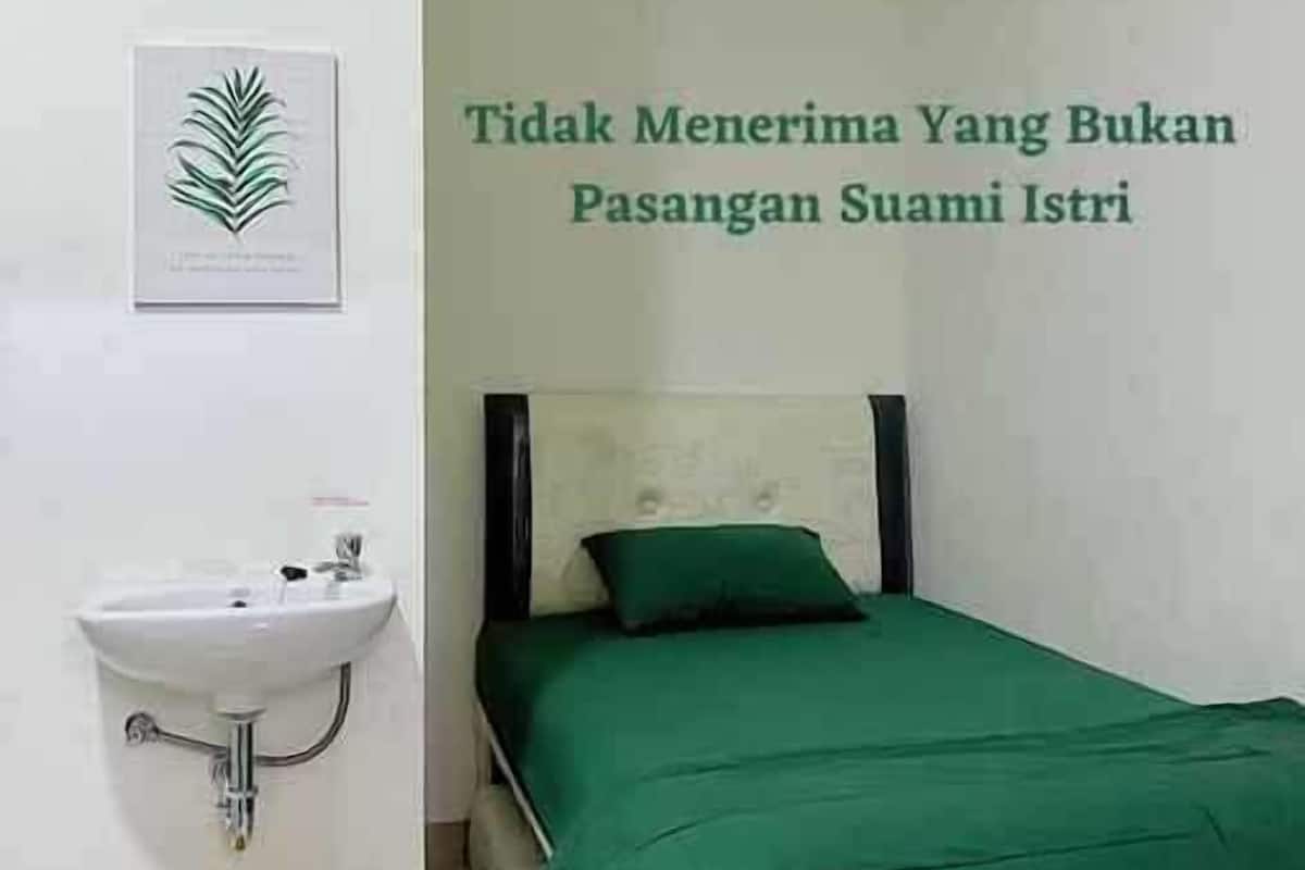 A small, clean room with a bed, a sink, and a trash bin.