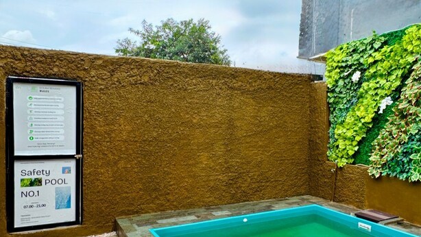 A small outdoor pool with a safety sign, surrounded by stone tiles and a textured wall. - ANUGRAH INN HOTEL (Ciakar)