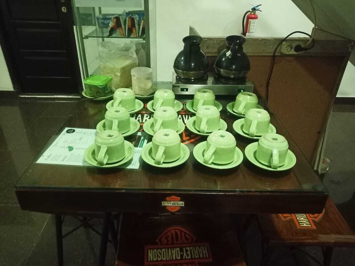 A table with multiple green cups and saucers, a menu, and a coffee maker.