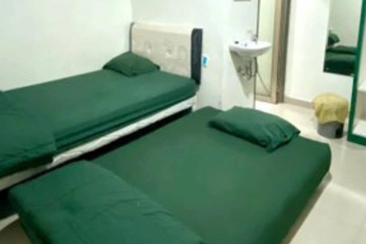 A room with two single beds, a small bedside table, a mirror, and a sink.