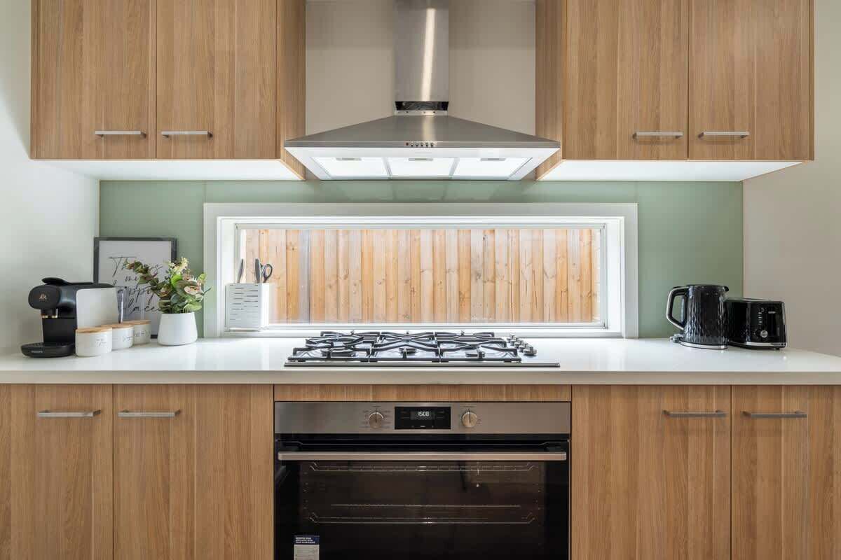 Une cuisine moderne avec des meubles en bois, une hotte en acier inoxydable, un four encastré et une fenêtre offrant une belle vue.