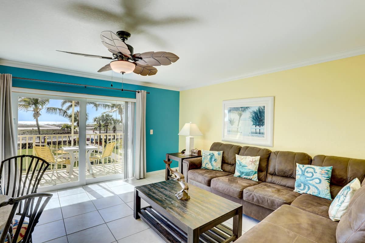 A living room with a sofa, a coffee table, a ceiling fan, and a view through a sliding glass door.