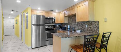 A kitchen with stainless steel appliances, granite countertops, wooden cabinets, and a bar area with two chairs.