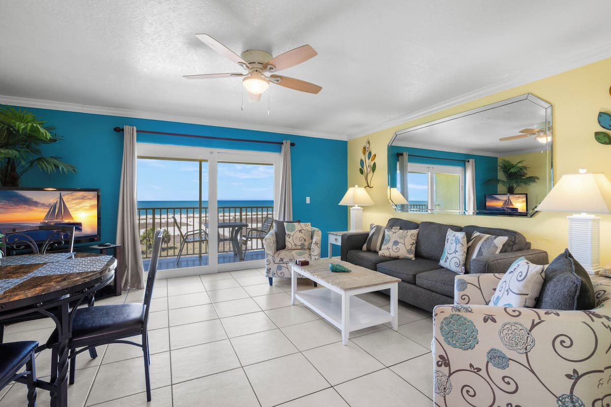 A living room with a balcony, a ceiling fan, a sofa, a coffee table, and a dining table with chairs.