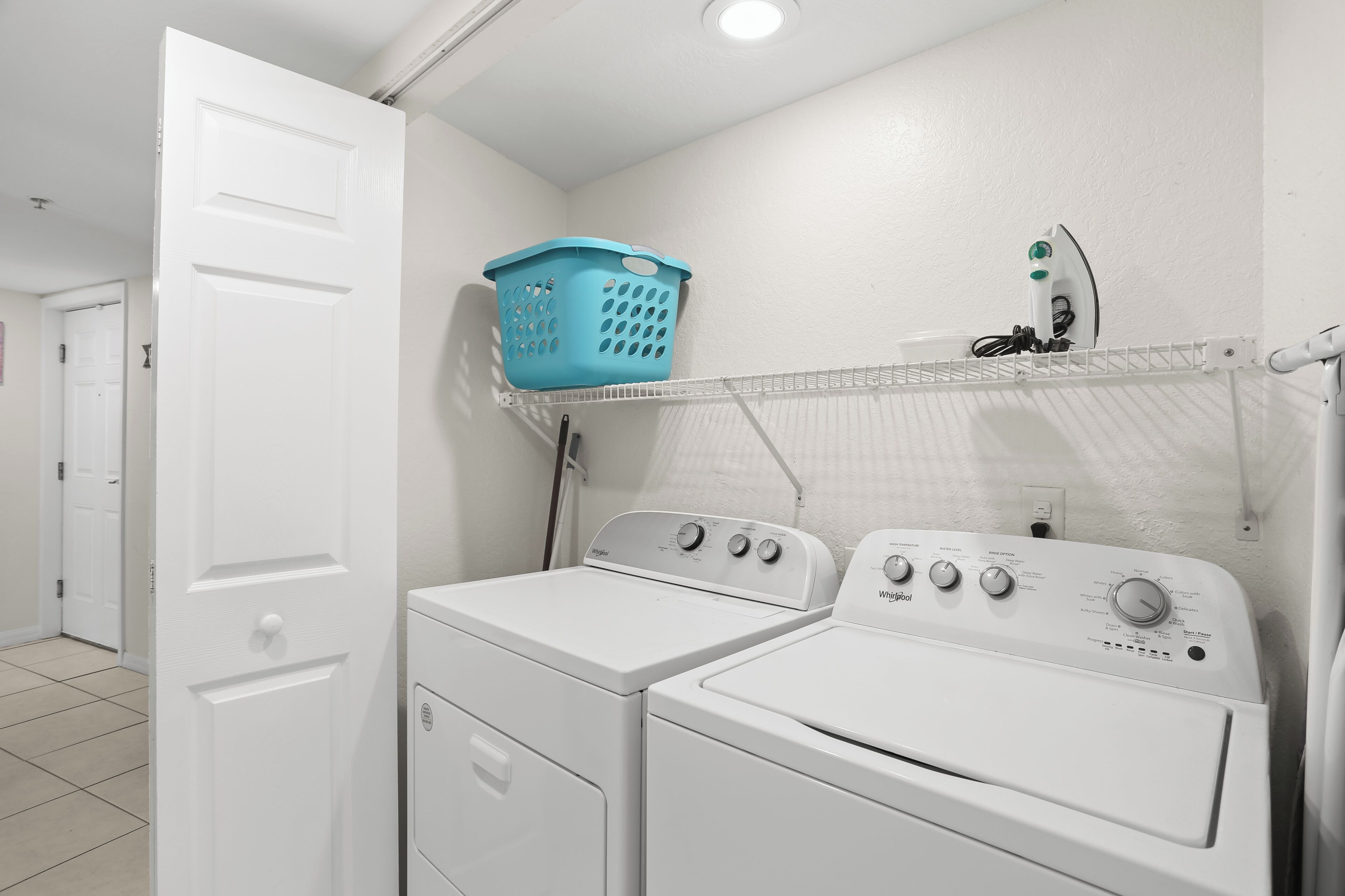 A laundry area with two white washing machines, a blue laundry basket on a rack, and a white door.