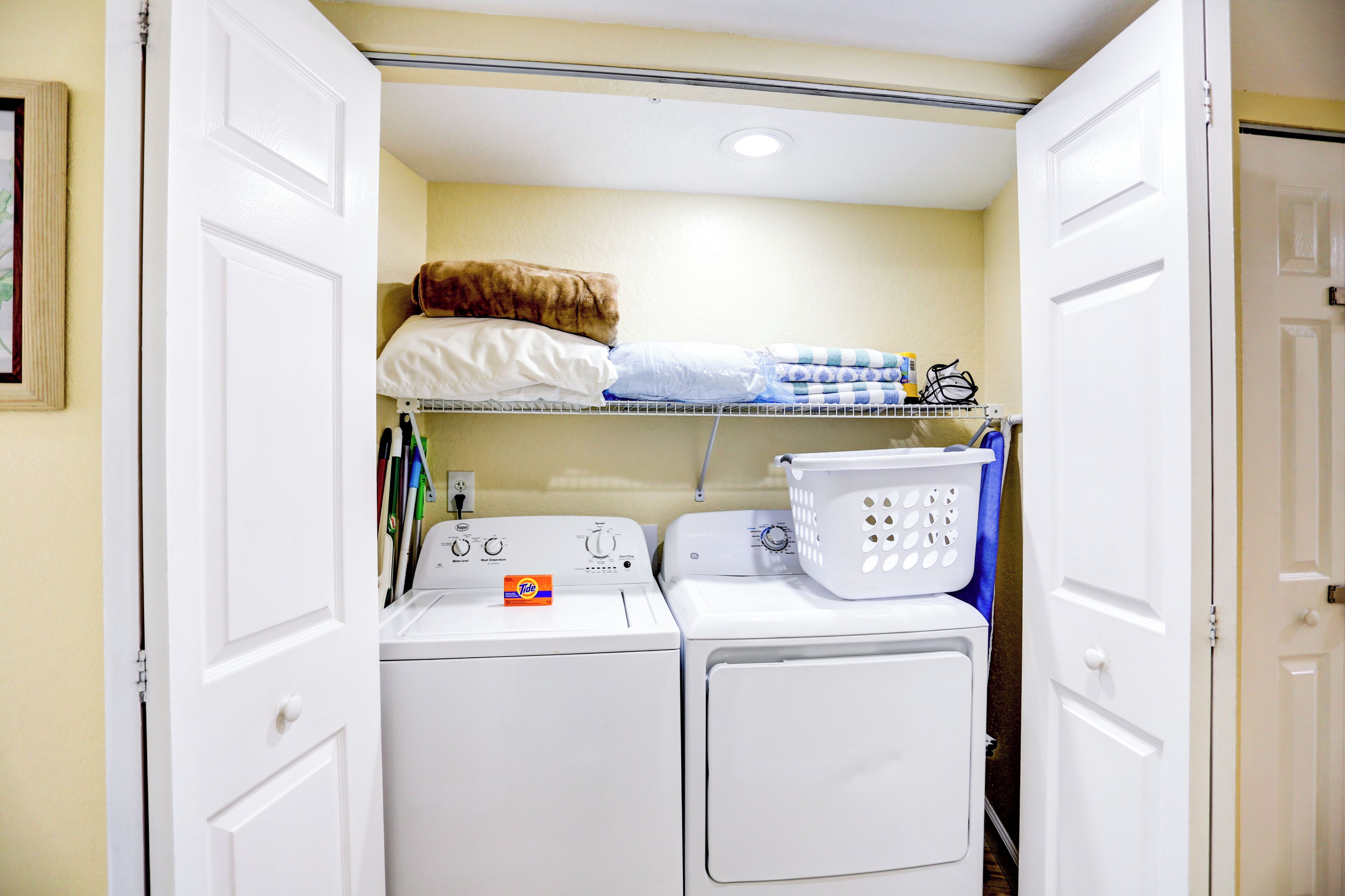 A laundry room with two stacked washers and dryers, a shelf with folded laundry, and a basket on the dryer.