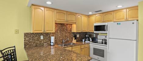 Una cocina con encimeras de granito, armarios de madera, un refrigerador blanco y un microondas integrado.