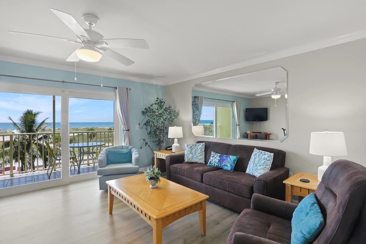 A living room with a balcony, a ceiling fan, a sofa, a coffee table, and a TV.