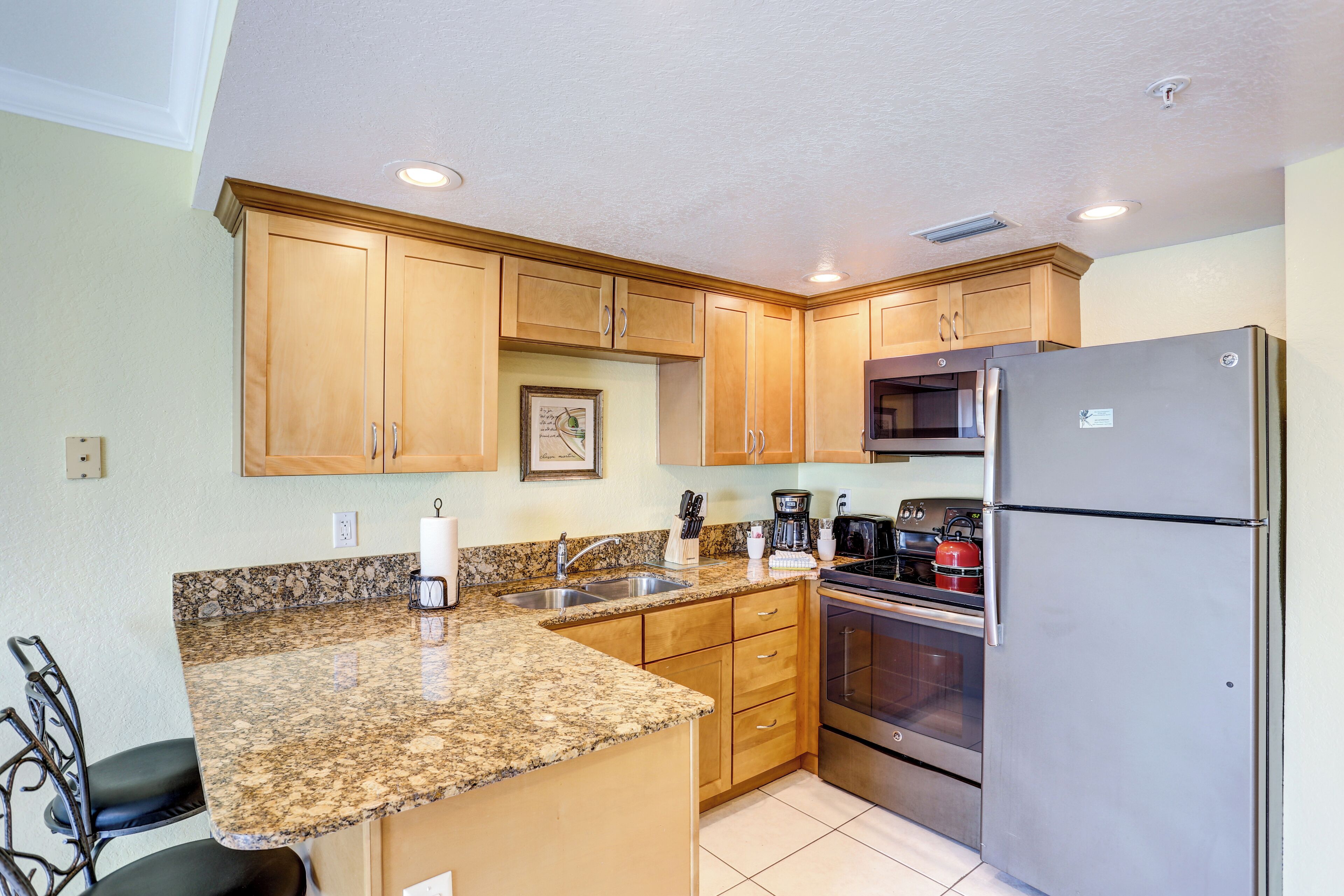 A kitchen with granite countertops, wooden cabinets, stainless steel appliances, and a dining area with chairs.