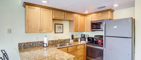 A kitchen with granite countertops, wooden cabinets, stainless steel appliances, and a dining area with chairs.