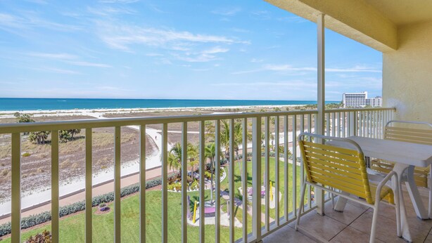 A balcony with a view of the beach and ocean, a table, and yellow chairs. - South Beach Condo Hotel (Treasure Island)
