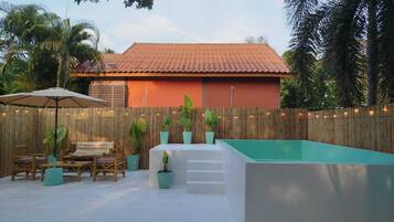 A backyard with a swimming pool, wooden deck, outdoor furniture, and a bamboo fence.