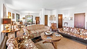 Un salon spacieux avec un canapé à rayures, un canapé à motifs floraux et une table basse ronde. On y trouve également un meuble en bois et une lampe sur une table d’appoint.