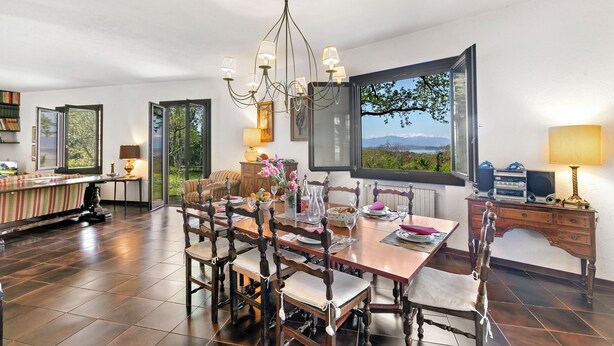 Un espace repas comprenant une table et des chaises en bois, un lustre et une grande fenêtre donnant sur l’extérieur.