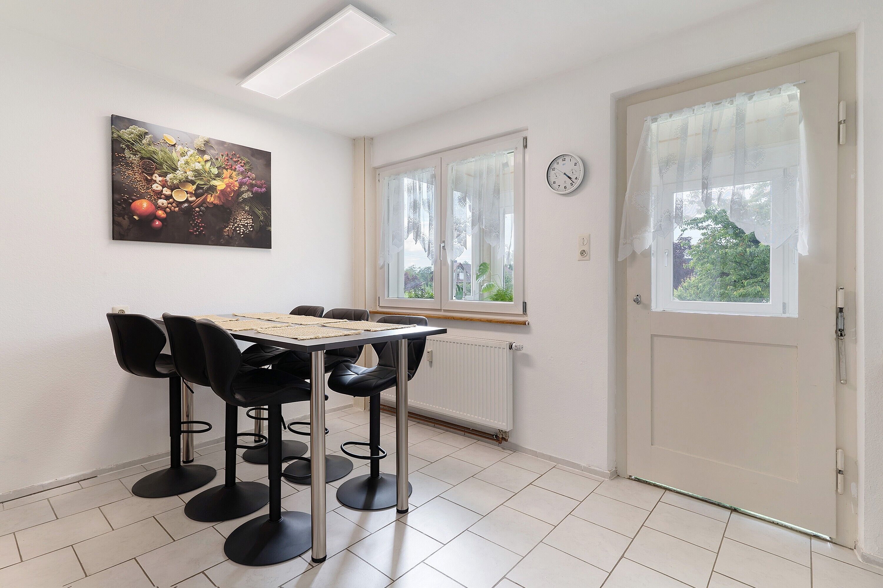 Et spiseområde med et bord, stole, et ur på væggen og en dør med et vindue.