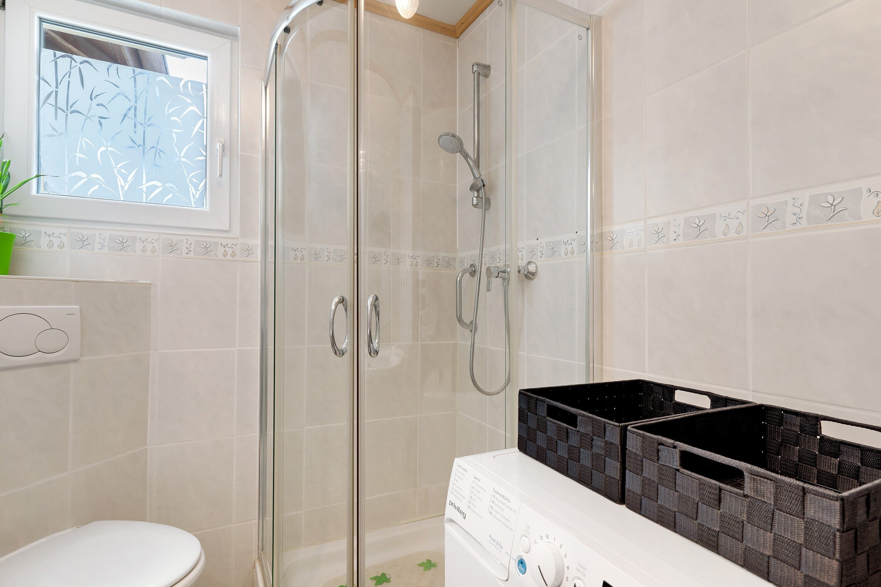 Un bagno con box doccia in vetro, un water bianco e una lavatrice.