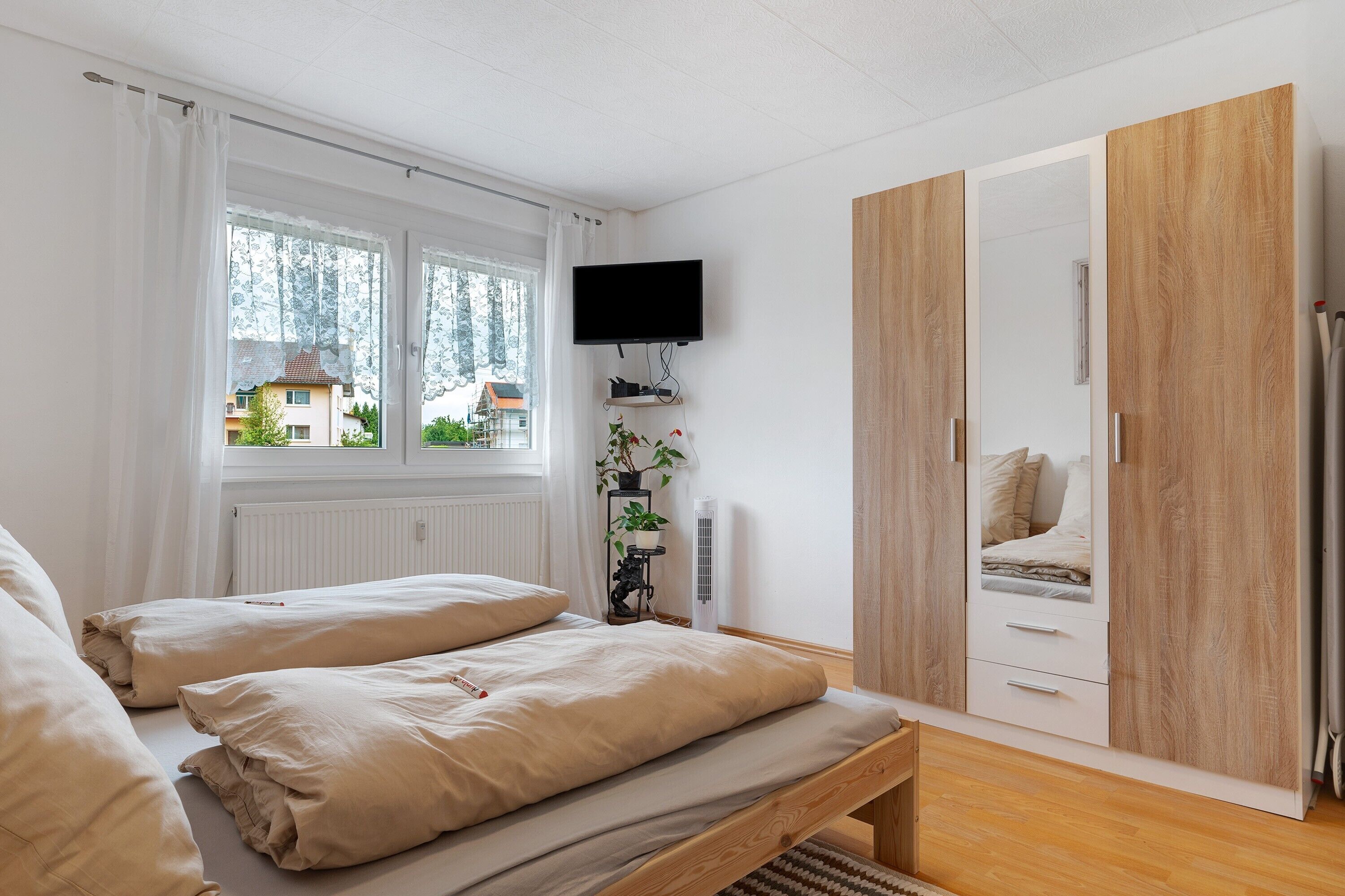 Een slaapkamer met een bed, een televisie, een kledingkast en een raam met gordijnen.
