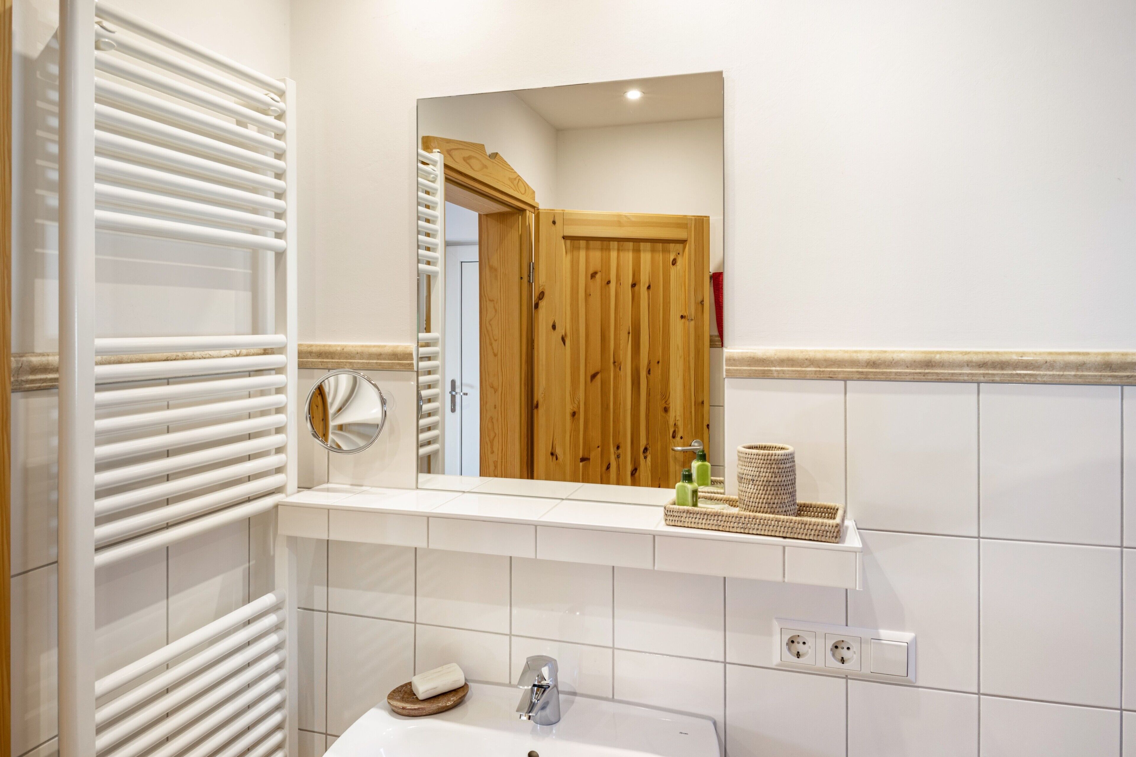 A bathroom with a white tiled wall, a white sink, a mirror, and a wooden door.