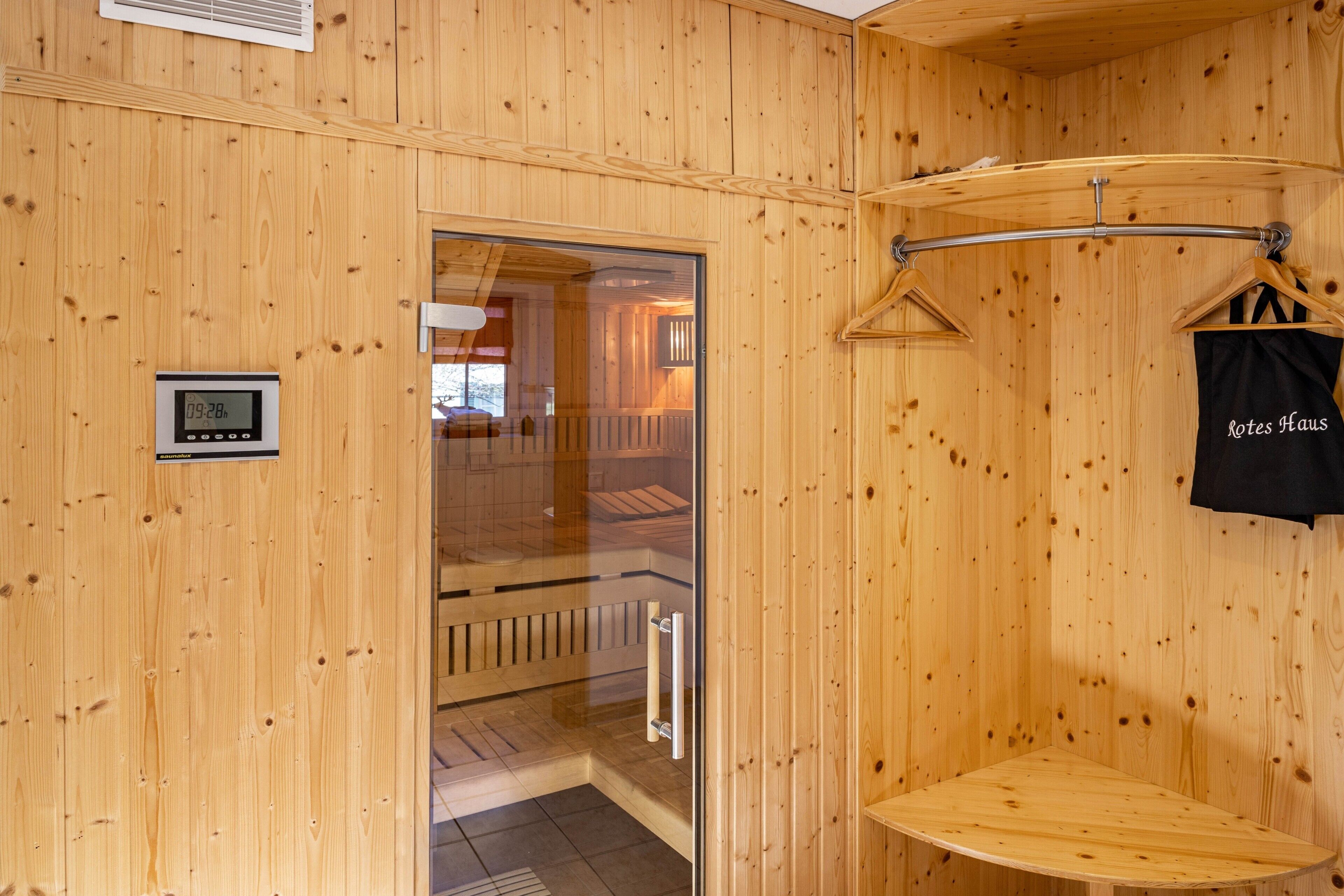 A wooden sauna room with a glass door, a digital clock, and a towel rack.
