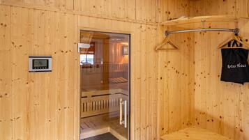 A wooden sauna room with a glass door, a digital clock, and a towel rack.