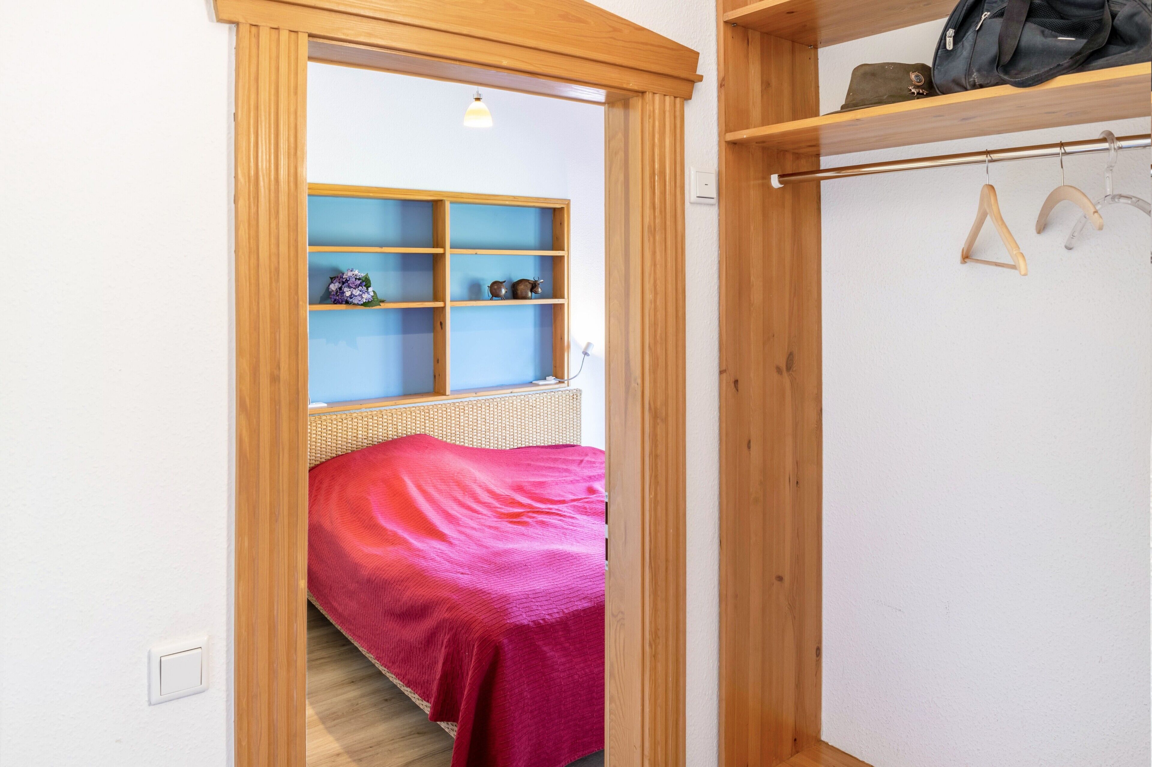 Een slaapkamer met een bed, een houten garderobe, een plank met spullen en een kledingroede.