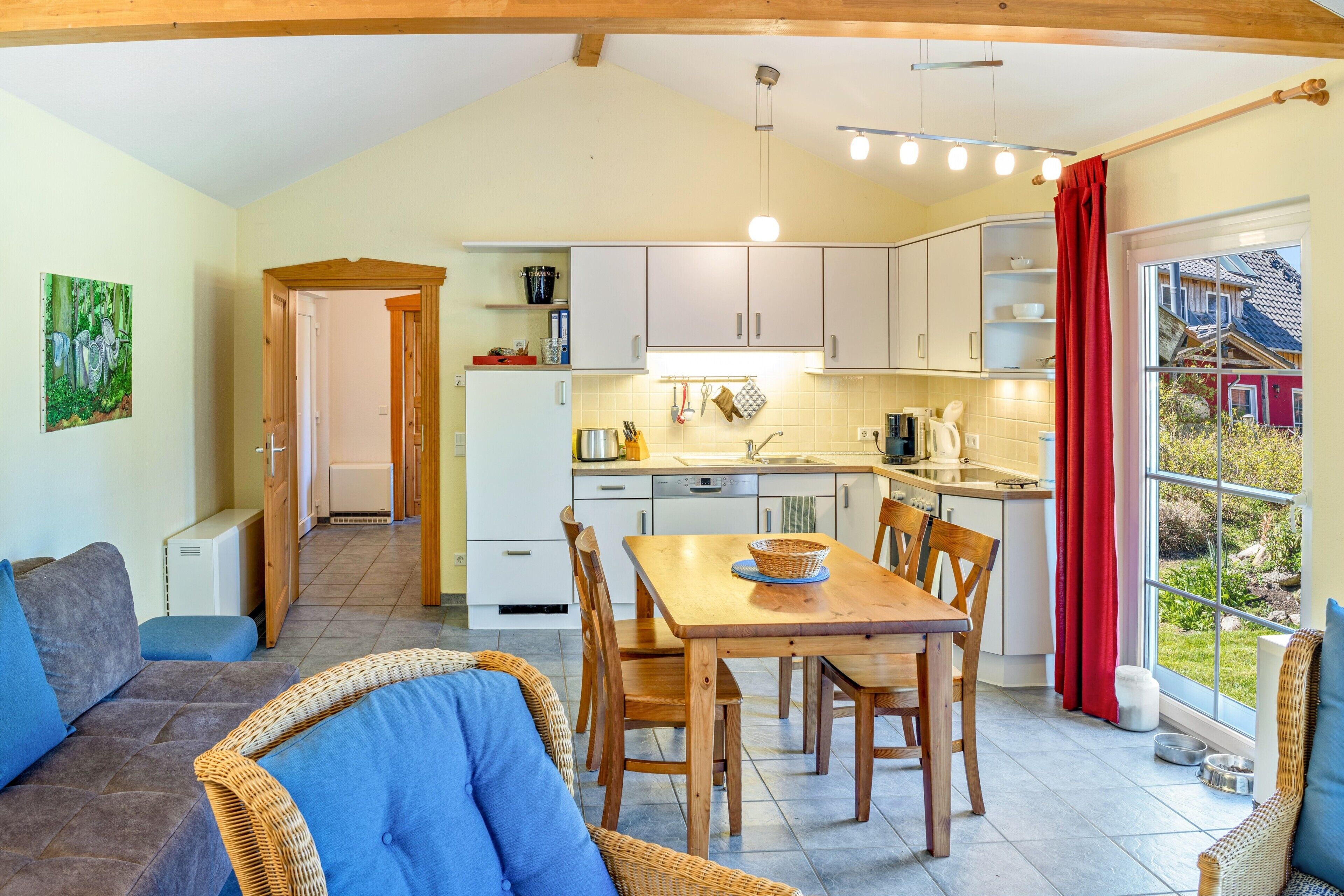 A cozy kitchen with a dining area, wooden furniture, and a view through a large window.