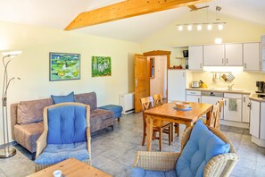 A cozy living room with a sofa, chairs, a dining table, and a kitchen area with cabinets and a sink.