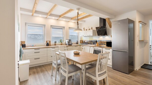 Una cocina moderna con muebles blancos, una mesa de comedor de madera y un refrigerador empotrado.