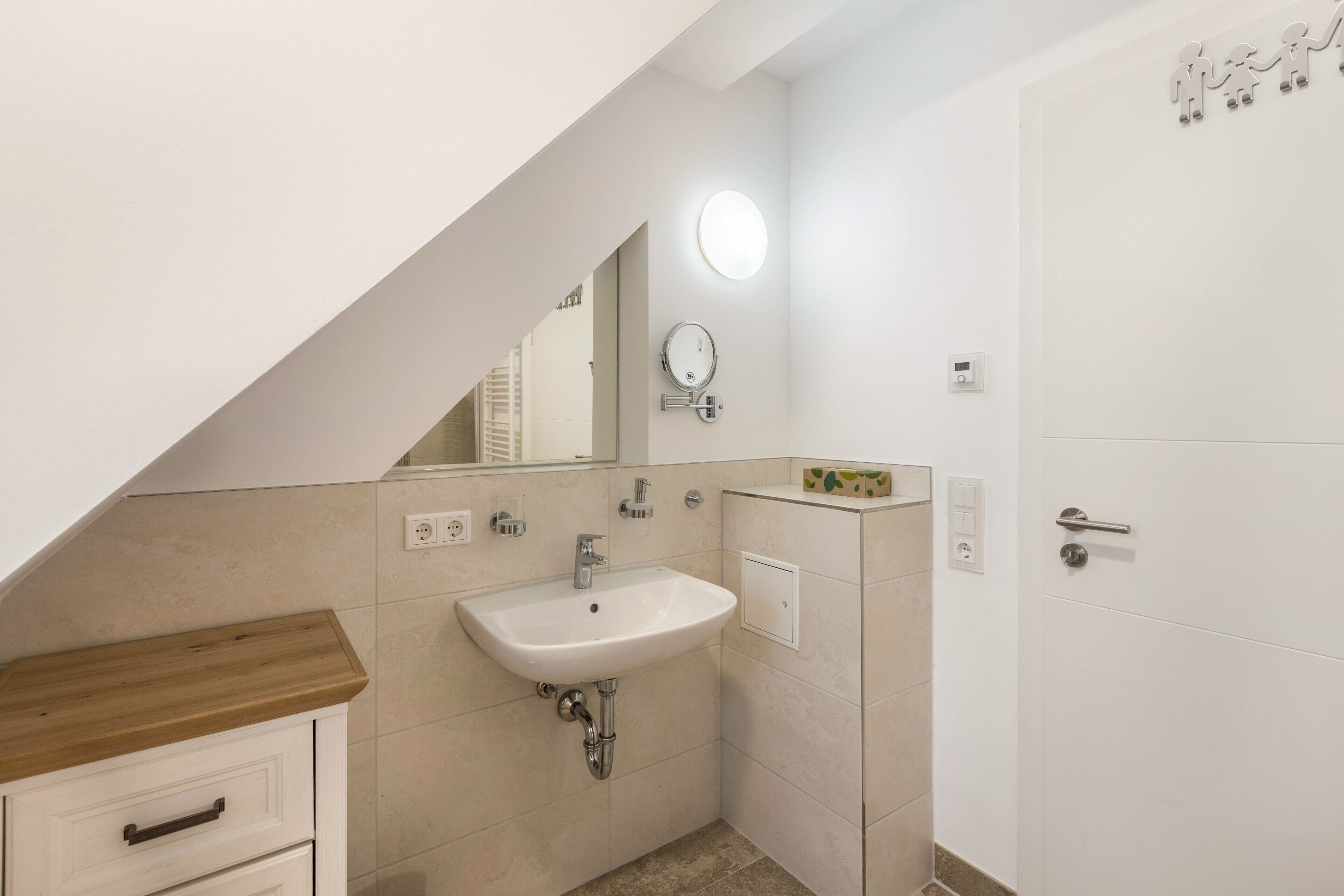 Un bagno con lavandino bianco, specchio e porta, oltre a un piano d'appoggio in legno.