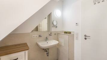 Un bagno con lavandino bianco, specchio e porta, oltre a un piano d'appoggio in legno.