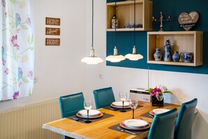 Un coin repas avec une table en bois, des chaises bleues et des lampes suspendues.