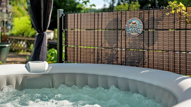 An outdoor hot tub with a wooden fence and a sign that reads 'POOL ZONE SUMMER.'
